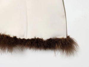 Detail of off-white satin dress featuring premium dark brown feather trim on the hemline