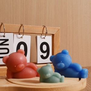 Three colorful sleepy bear candles in a rustic wooden tray with a wooden calendar setup