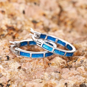 Dettaglio macro di orecchini geometrici in argento con pietre di opale blu su roccia