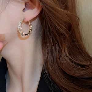 Close-up of gold C-shaped hoop earrings with pave-set zircon on an ear lobe