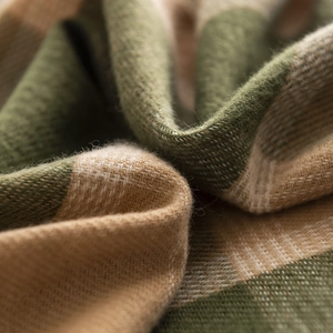 Detailed macro shot of soft green and beige plaid cashmere texture on a warm scarf