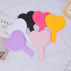 Flat lay of heart-shaped handheld makeup mirrors in various pastel colors on a white rug