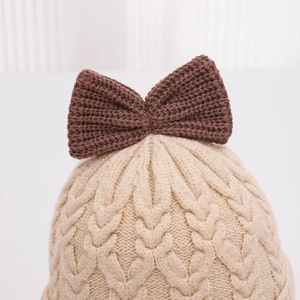 Dettaglio di un cappello invernale per neonati con trama a treccia e fiocco marrone.
