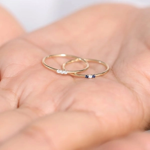 Macro shot of minimalist 18K gold band rings with blue and white stones on palm