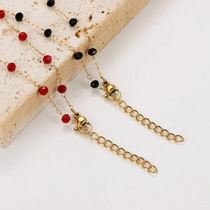 Gros plan d'un collier en acier doré avec des perles facettées rouges et noires