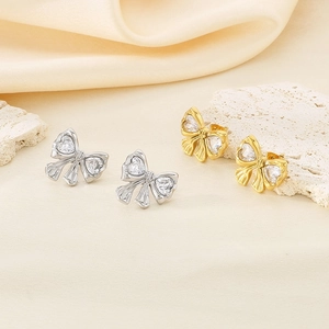 Detail view of 18K gold and silver bow stud earrings with heart zirconia accents