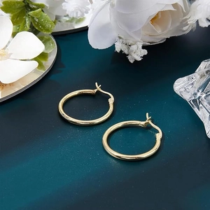 Classic gold hoop earrings showcased on a textured teal background with floral accents