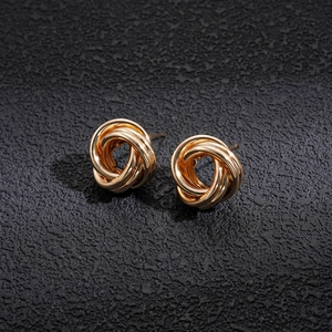 Detail shot of golden multi-loop intertwined knot earrings on textured grey background