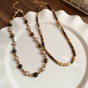 Macro detail of Tiger Eye and pearl beaded necklaces on a white decorative ceramic plate