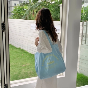 Close-up of light blue canvas tote bag with yellow PARIS embroidery in outdoor garden