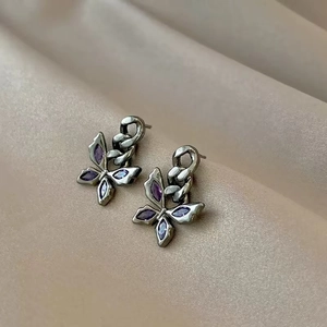 Detailed macro of vintage silver butterfly earrings with purple crystals on champagne silk