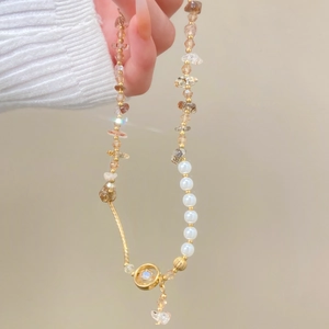 Détail de bracelet perlé avec cristaux bruns, perles blanches et pendentif papillon