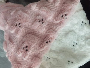 Close-up of pink and white plush fabric with cute cartoon animal embroidery and soft texture