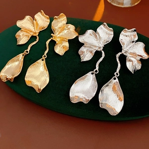 Detailed view of metal flower earrings in gold and silver finish on velvet tray