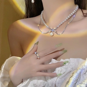 Double-layered pearl bow necklace and crystal ring set worn by model in warm lighting