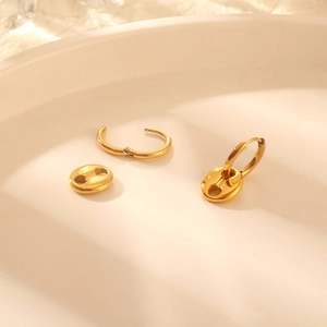 Detailed view of gold pig nose anchor chain earrings on a minimalist white tray