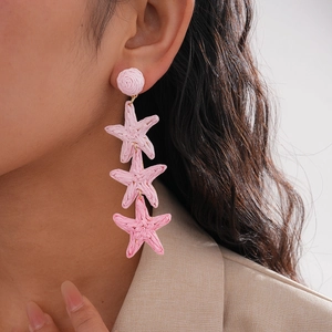 Close-up of model wearing pink raffia woven triple starfish drop earrings for summer