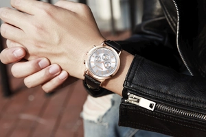 Close-up of rose gold chronograph watch with black leather strap worn with jacket