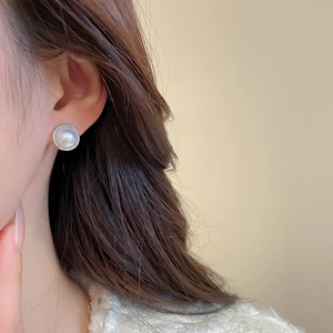Macro view of a pearl stud earring with silver metal edge worn on a model's ear