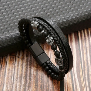 Close-up of multilayer black leather and woven rope bracelet with metal skull charms
