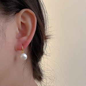 Detailed view of a round freshwater pearl earring with a minimalist gold hook on the ear