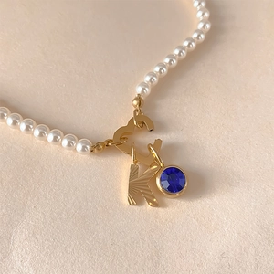 Gros plan détaillé d'un collier de perles avec lettre K dorée et pendentif bleu