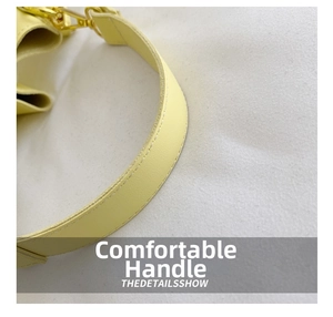 Macro detail of yellow leather bucket bag handle with golden metal buckle and stitching