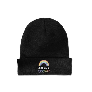 Détail d'un bonnet noir en maille avec broderie arc-en-ciel, texte SMILE et cœurs colorés