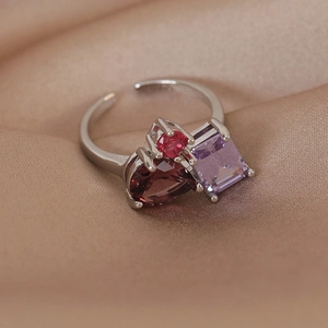 Macro shot of silver open ring featuring pear red, square purple, and pink gemstones