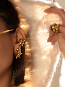 Detailed close-up of chunky gold C-shape sunburst earrings and minimalist ring set