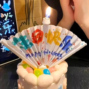 Close-up of a lit fan-shaped birthday candle with colorful Happy Birthday text on a cake