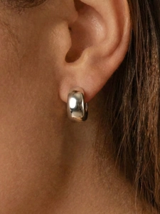 Gros plan de boucles d'oreilles créoles en C en acier poli sur l'oreille d'un mannequin