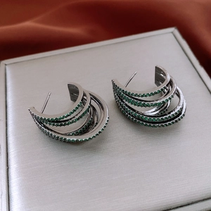 Vue macro de boucles d'oreilles multicouches serties de zircons verts sur métal argent foncé
