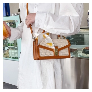 Detail of straw shoulder bag with brown PU leather flap, metal lock and silk scarf decor