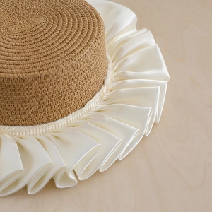 Straw boater hat with elegant white satin ruffled brim on a light wood background