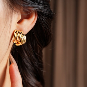 Close-up of golden geometric interlaced hoop earrings worn by a model in soft lighting