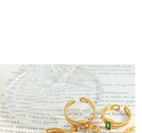 Detailed view of gold textured open rings with green and clear gemstones on vintage paper