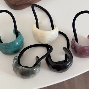 Five assorted marble pattern acetate hair ties with black elastic bands on white surface