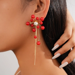 Macro view of red pearl flower earrings with long gold tassel fringe on a female model