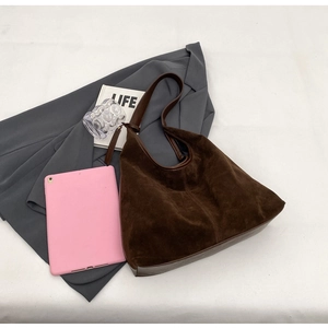 Flat lay of brown suede hobo bag with leather strap, tablet, and fashion accessories