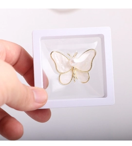 Detail of white butterfly brooch with pearl in a PE film suspension display box