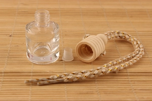 Detail of 8ml clear glass car perfume bottle with wooden cap and woven lanyard on bamboo mat