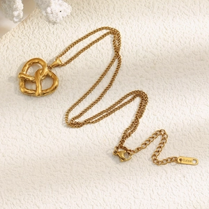 Detail of 18K gold plated stainless steel heart knot pendant on a textured surface