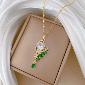 Close-up of a gold-plated peacock pendant with white crystals and green drop gemstones
