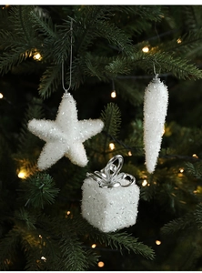 Close-up of white glitter star and gift box ornaments on a lighted Christmas tree