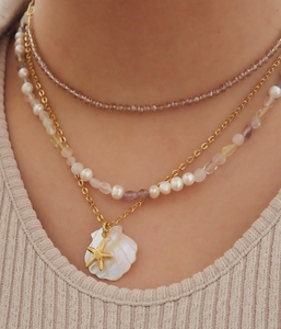 Close-up of a three-layer gold necklace featuring purple beads, pearls, and starfish charms