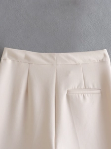 Detailed view of the pleated waistband and rear pocket on off-white straight leg trousers