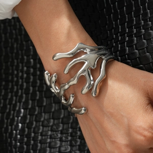 Detailed view of silver liquid metal cuff bracelet on wrist against dark leather texture