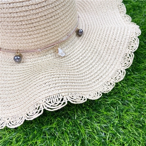 Détail d'un chapeau de paille avec bords en dentelle, perles grises et pendentif coquillage
