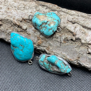 Macro shot of irregular turquoise stone pendants with metal edging on natural bark background